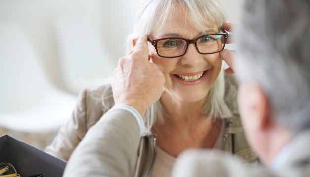 Séniore souriante essaie des lunettes chez l'opticien et bénéficie de tarifs négociés
